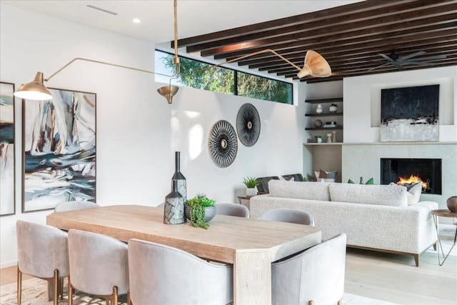 dining room with recessed lighting, a warm lit fireplace, and wood finished floors
