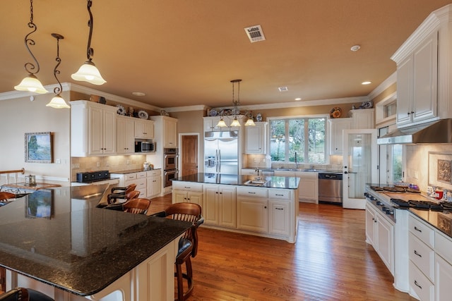 kitchen featuring stainless steel appliances, white cabinetry, a center island, wood-type flooring, and decorative backsplash