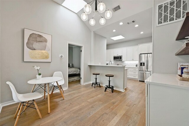 kitchen with white cabinets, decorative light fixtures, light hardwood / wood-style flooring, a chandelier, and appliances with stainless steel finishes