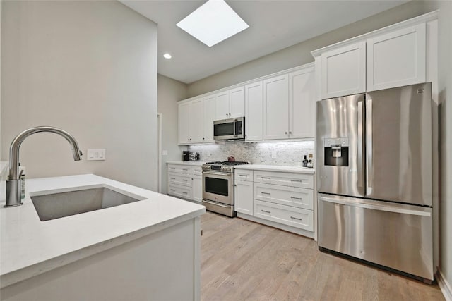 kitchen with white cabinets, a skylight, stainless steel appliances, and sink