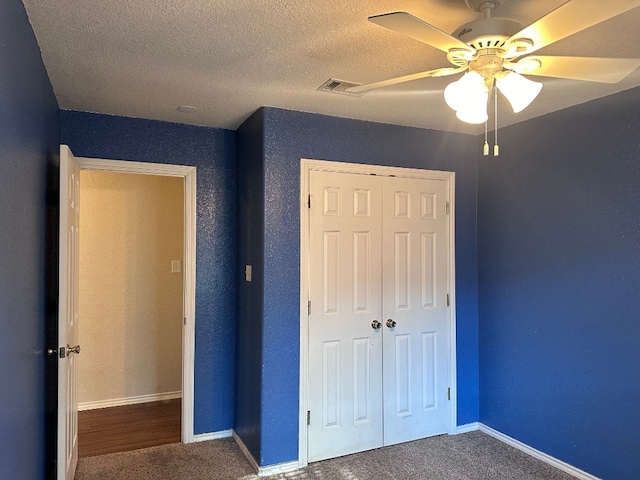 unfurnished bedroom with a closet, ceiling fan, carpet floors, and a textured ceiling