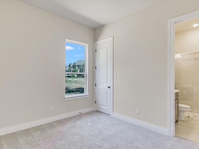 unfurnished bedroom with ensuite bathroom, multiple windows, and light colored carpet