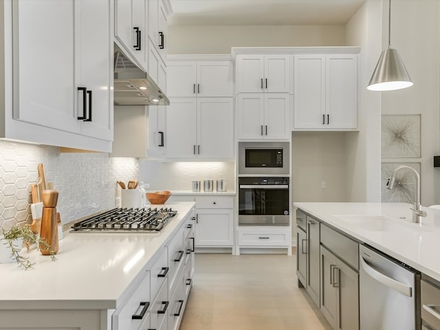 kitchen with wall chimney range hood, pendant lighting, backsplash, stainless steel appliances, and sink