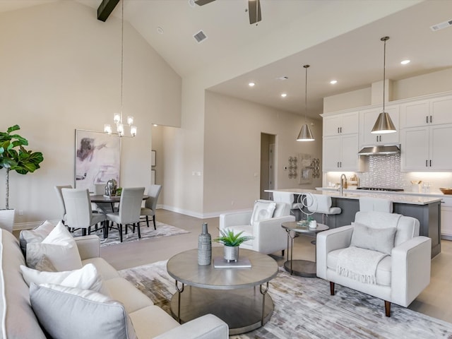 living room with beamed ceiling, high vaulted ceiling, ceiling fan with notable chandelier, and light hardwood / wood-style floors