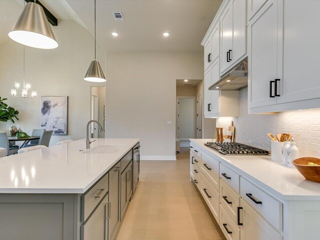 kitchen with tasteful backsplash, a center island with sink, light wood-type flooring, pendant lighting, and white cabinetry