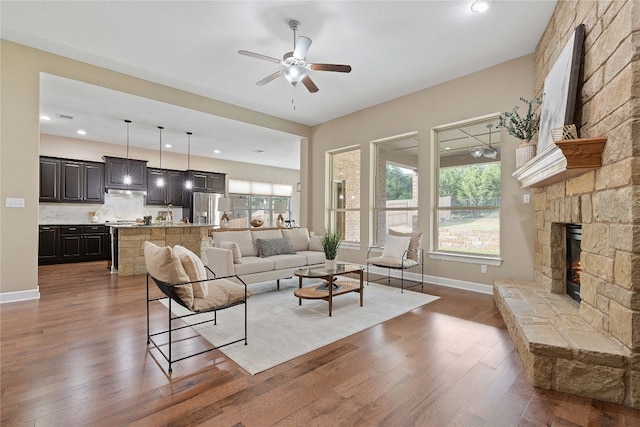 living room with dark hardwood / wood-style flooring, a stone fireplace, and ceiling fan