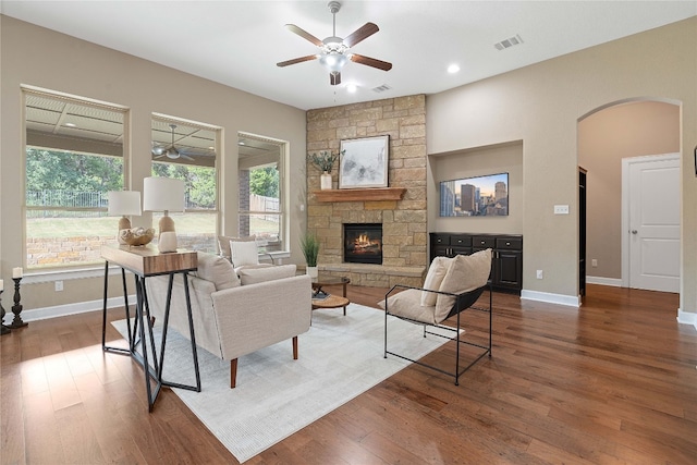 living room featuring ceiling fan, a fireplace, dark wood-type flooring, and a wealth of natural light