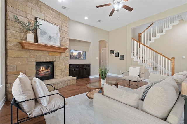 living room featuring ceiling fan, a stone fireplace, and wood-type flooring