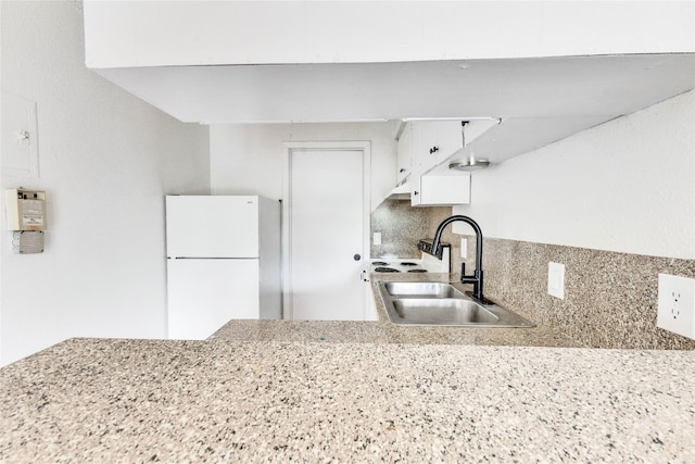 kitchen with decorative backsplash, white cabinetry, white refrigerator, light stone countertops, and sink