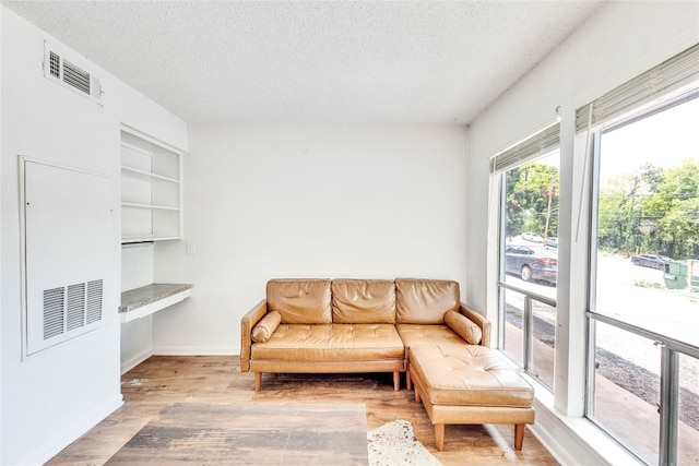 living room with a textured ceiling, built in features, and light hardwood / wood-style floors