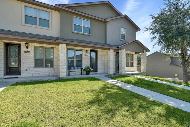 townhome / multi-family property with stone siding, a shingled roof, a front lawn, and stucco siding