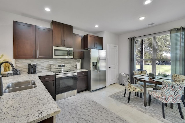 kitchen with appliances with stainless steel finishes, tasteful backsplash, sink, light stone countertops, and light tile patterned floors