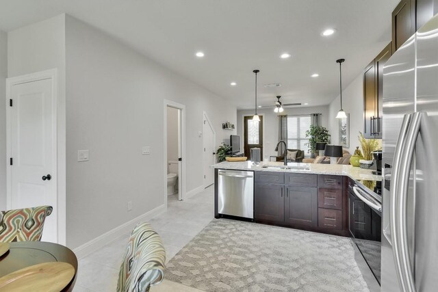 kitchen with ceiling fan, dark brown cabinetry, appliances with stainless steel finishes, light stone countertops, and sink