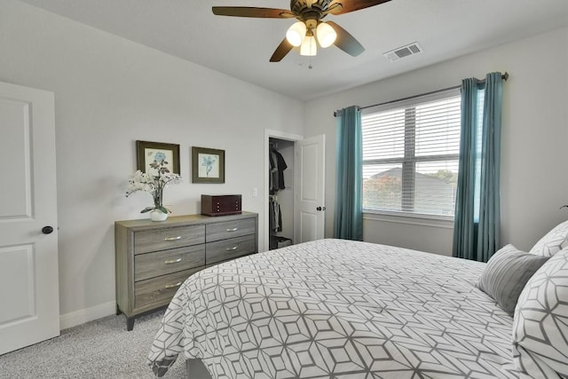 bedroom featuring light colored carpet, visible vents, a spacious closet, a ceiling fan, and baseboards