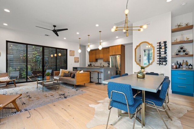 dining room with ceiling fan with notable chandelier, built in shelves, and light hardwood / wood-style floors