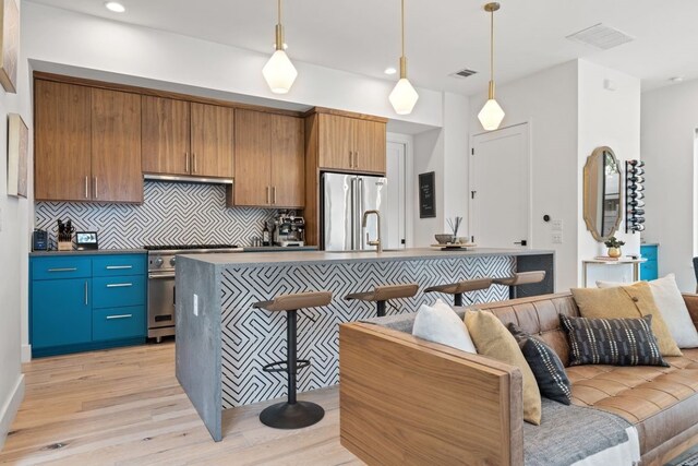 kitchen with an island with sink, high quality fridge, backsplash, light hardwood / wood-style floors, and range