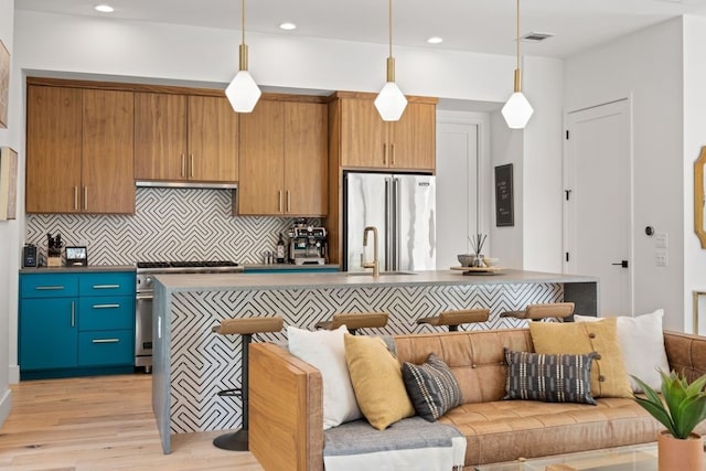 kitchen with stainless steel appliances, dark countertops, a center island with sink, and pendant lighting