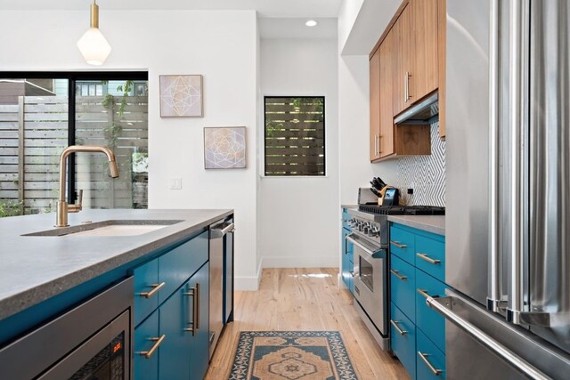 kitchen with blue cabinets, premium appliances, light hardwood / wood-style floors, backsplash, and sink