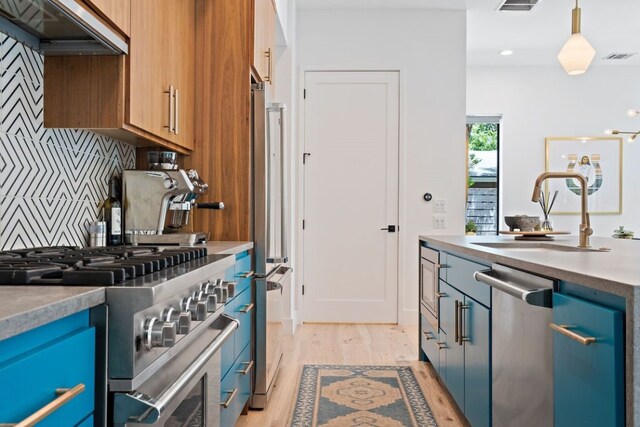 kitchen with decorative backsplash, stainless steel appliances, pendant lighting, light wood-type flooring, and premium range hood