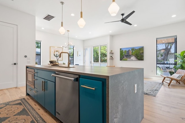 kitchen with ceiling fan with notable chandelier, appliances with stainless steel finishes, a center island with sink, sink, and light hardwood / wood-style floors