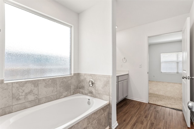 bathroom featuring tiled tub, vanity, and wood-type flooring