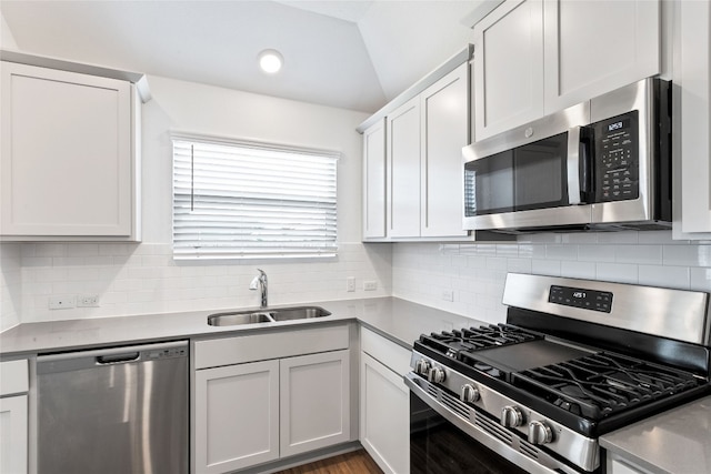 kitchen with decorative backsplash, stainless steel appliances, vaulted ceiling, sink, and white cabinets