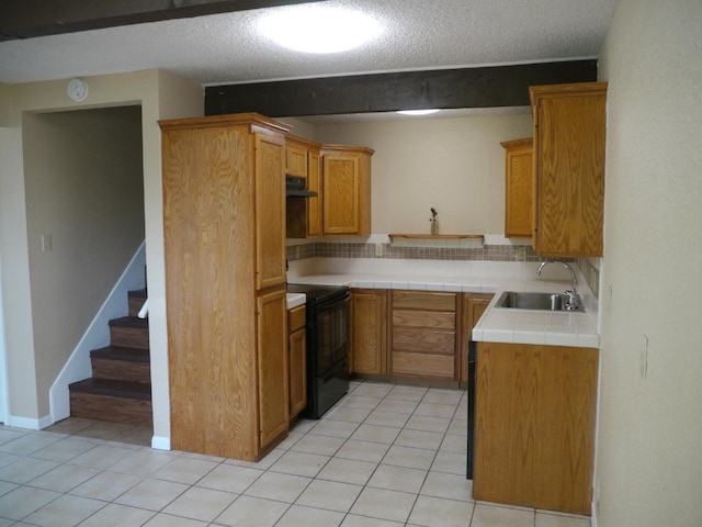 kitchen featuring black electric range oven, light tile patterned floors, tile counters, sink, and decorative backsplash