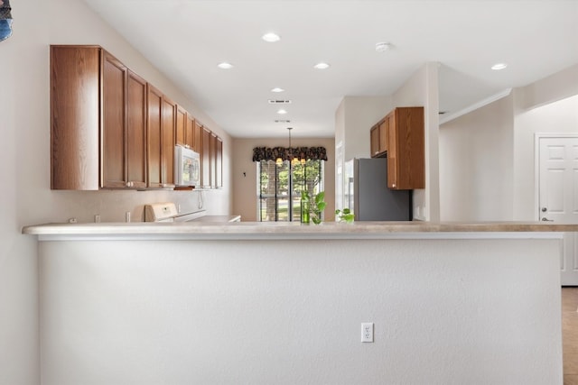 kitchen featuring an inviting chandelier, pendant lighting, kitchen peninsula, and stainless steel fridge