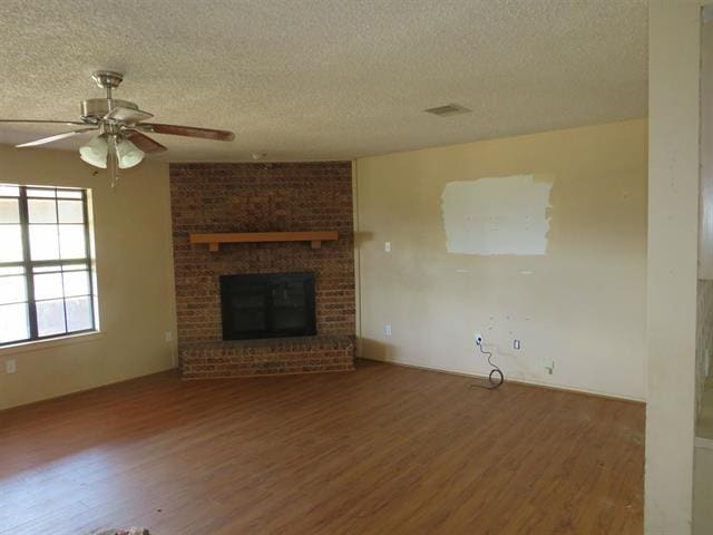 105 E Fawn Dr, Buchanan Dam, TX 78609 - unfurnished living room with a brick fireplace, ceiling fan, a textured ceiling, and dark wood-type flooring