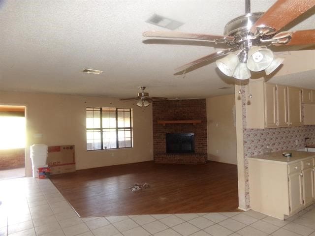 unfurnished living room featuring ceiling fan, a fireplace, brick wall, and light tile patterned floors