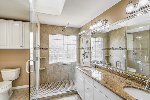 bathroom featuring tile patterned floors, dual bowl vanity, a shower with door, and toilet