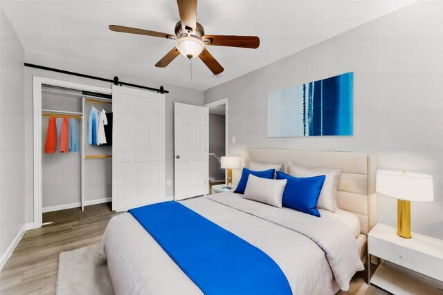 bedroom featuring ceiling fan, a barn door, a closet, and wood-type flooring