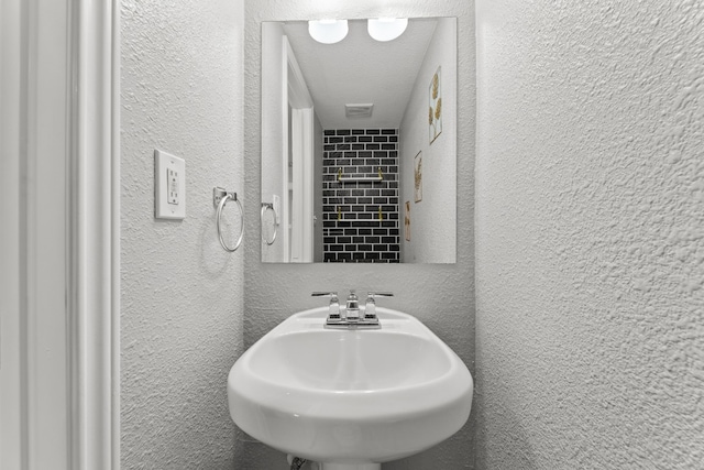 bathroom featuring a textured wall, a textured ceiling, and a sink