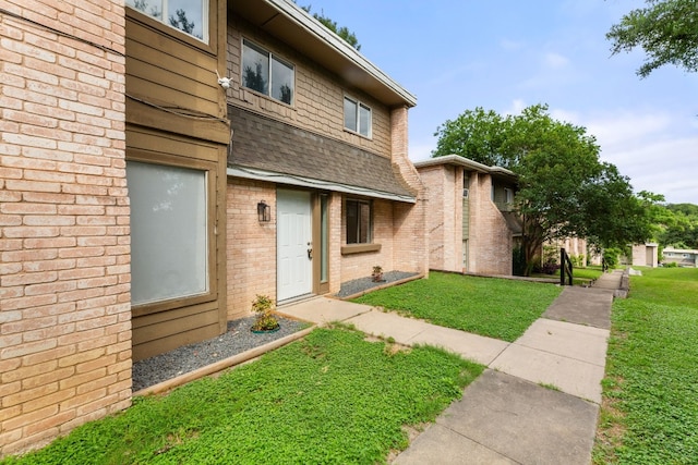 property entrance featuring a shingled roof, a lawn, and brick siding