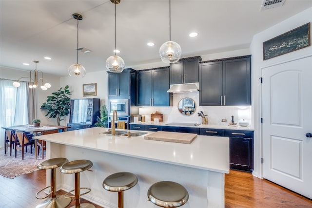 kitchen featuring decorative backsplash, appliances with stainless steel finishes, a center island with sink, light hardwood / wood-style floors, and sink