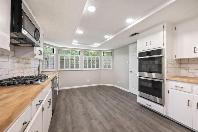 kitchen featuring appliances with stainless steel finishes, tasteful backsplash, butcher block countertops, white cabinets, and dark hardwood / wood-style flooring