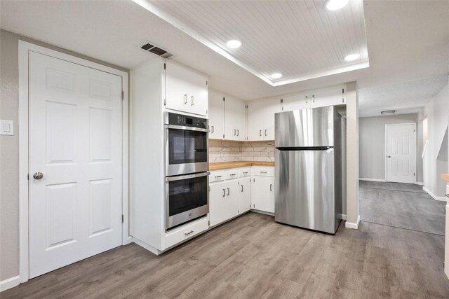 kitchen featuring appliances with stainless steel finishes, light hardwood / wood-style floors, white cabinets, wood counters, and backsplash