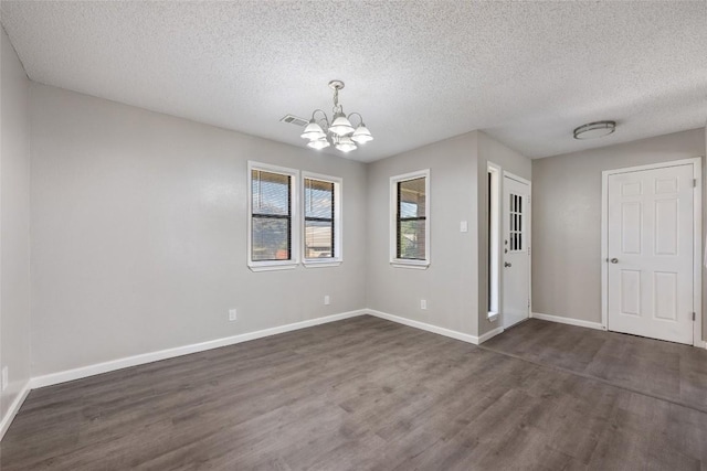 empty room with dark wood-type flooring, an inviting chandelier, and a textured ceiling