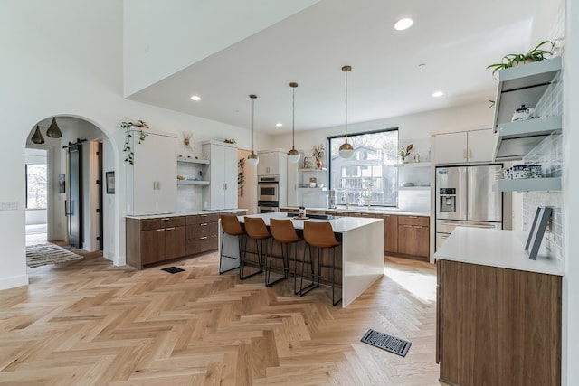 kitchen featuring appliances with stainless steel finishes, light parquet flooring, a center island, white cabinets, and a kitchen bar