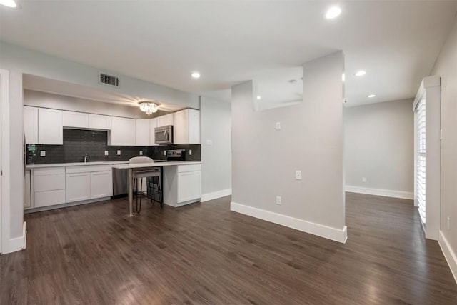935 La Posada Dr Unit 115, Austin, TX 78752 - kitchen featuring stainless steel microwave, decorative backsplash, white cabinetry, baseboards, and light countertops
