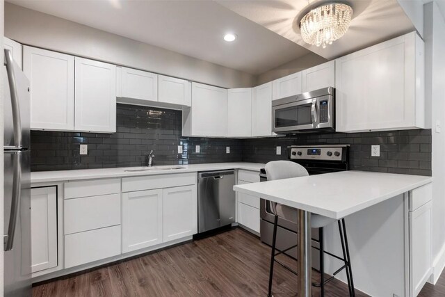 kitchen with dark wood-type flooring, appliances with stainless steel finishes, a kitchen breakfast bar, sink, and backsplash