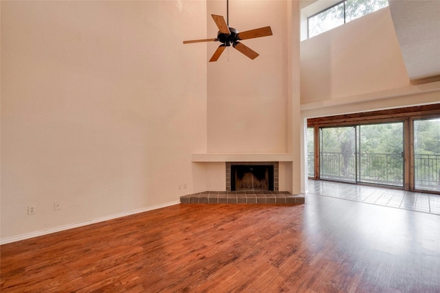 unfurnished living room featuring a tiled fireplace, ceiling fan, a towering ceiling, and hardwood / wood-style flooring