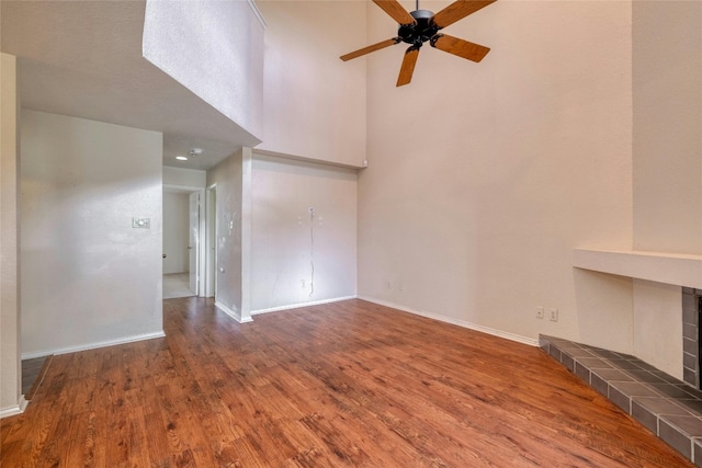 unfurnished living room with ceiling fan, dark hardwood / wood-style flooring, a fireplace, and a high ceiling