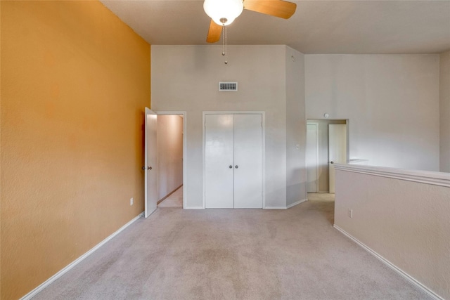 unfurnished bedroom with a towering ceiling, light colored carpet, a closet, and ceiling fan