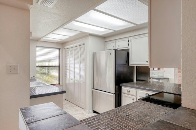 kitchen featuring white cabinets, stainless steel fridge, black cooktop, tile counters, and light tile patterned flooring