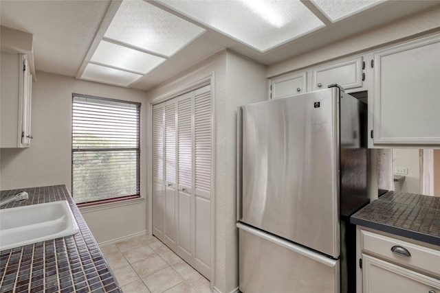 kitchen featuring tile counters, sink, light tile patterned floors, stainless steel fridge, and white cabinets