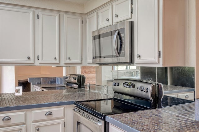 kitchen with tile countertops, white cabinetry, and appliances with stainless steel finishes