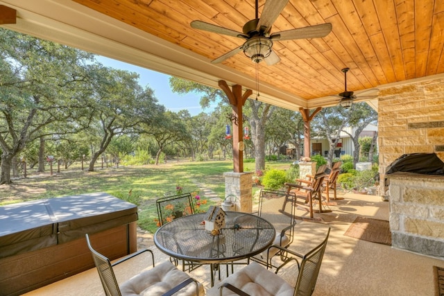 view of patio / terrace with a ceiling fan, outdoor dining area, an outdoor stone fireplace, and a hot tub