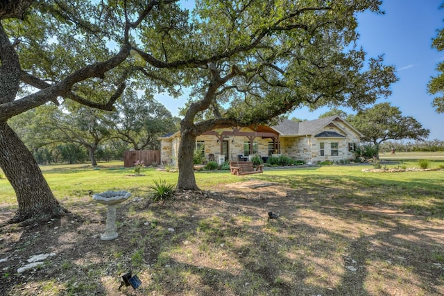 view of front facade with stone siding, a front lawn, and fence