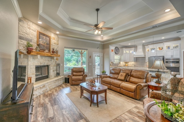 living area with visible vents, a raised ceiling, light wood-style flooring, ornamental molding, and a fireplace